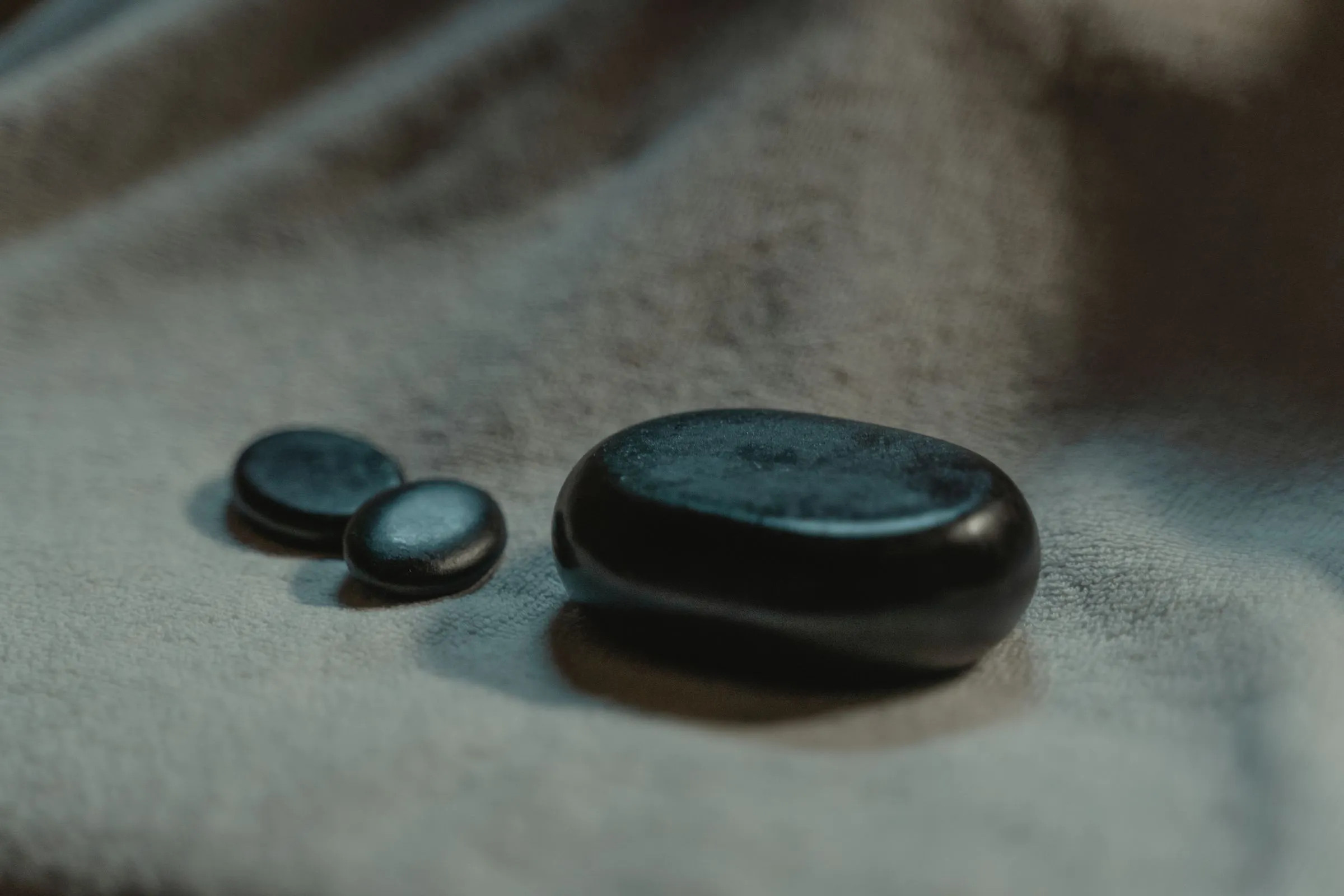 Smooth black massage stones resting on grey linen
