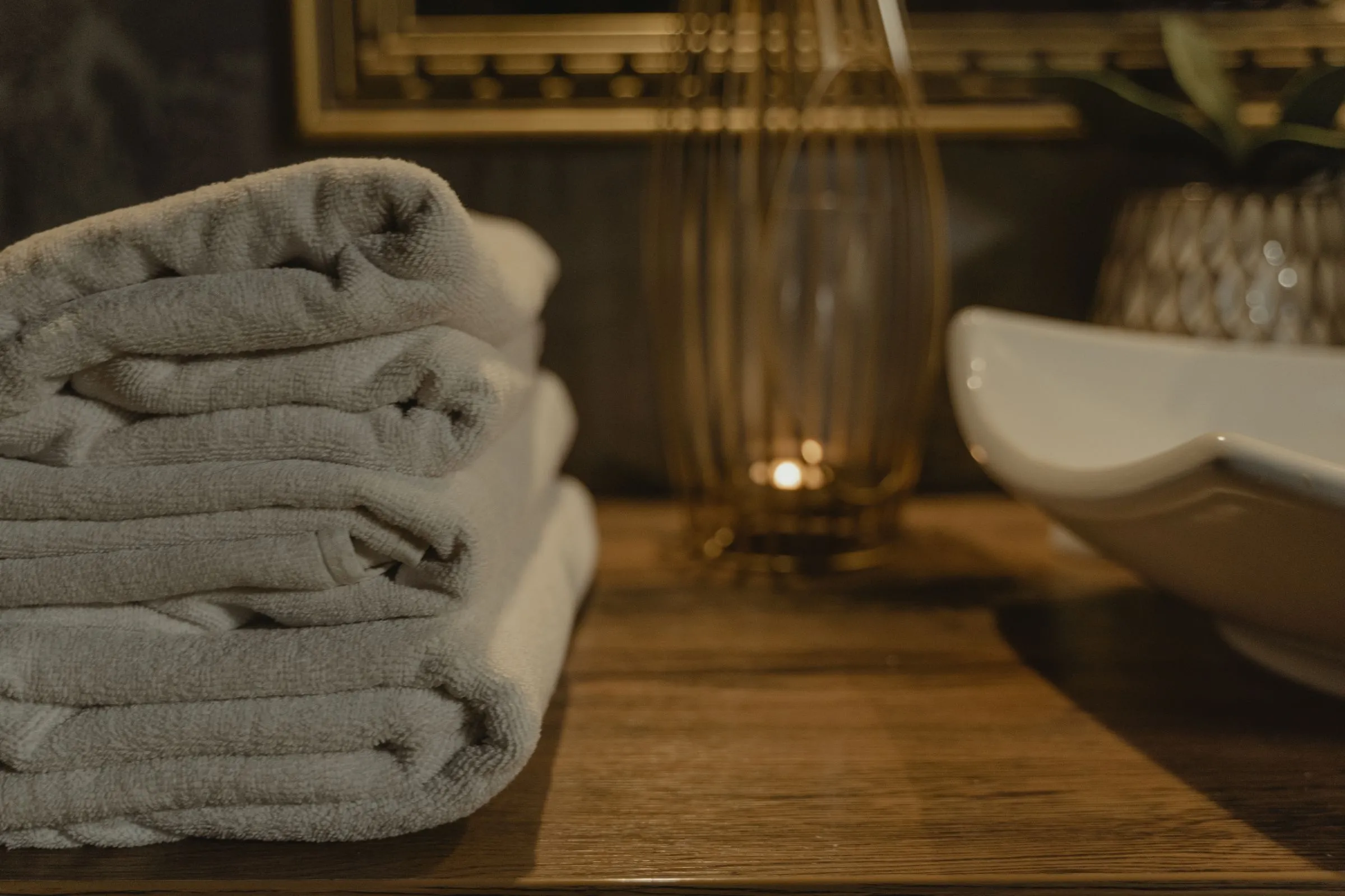 Soft grey towels folded on a wooden counter beside a lit candle