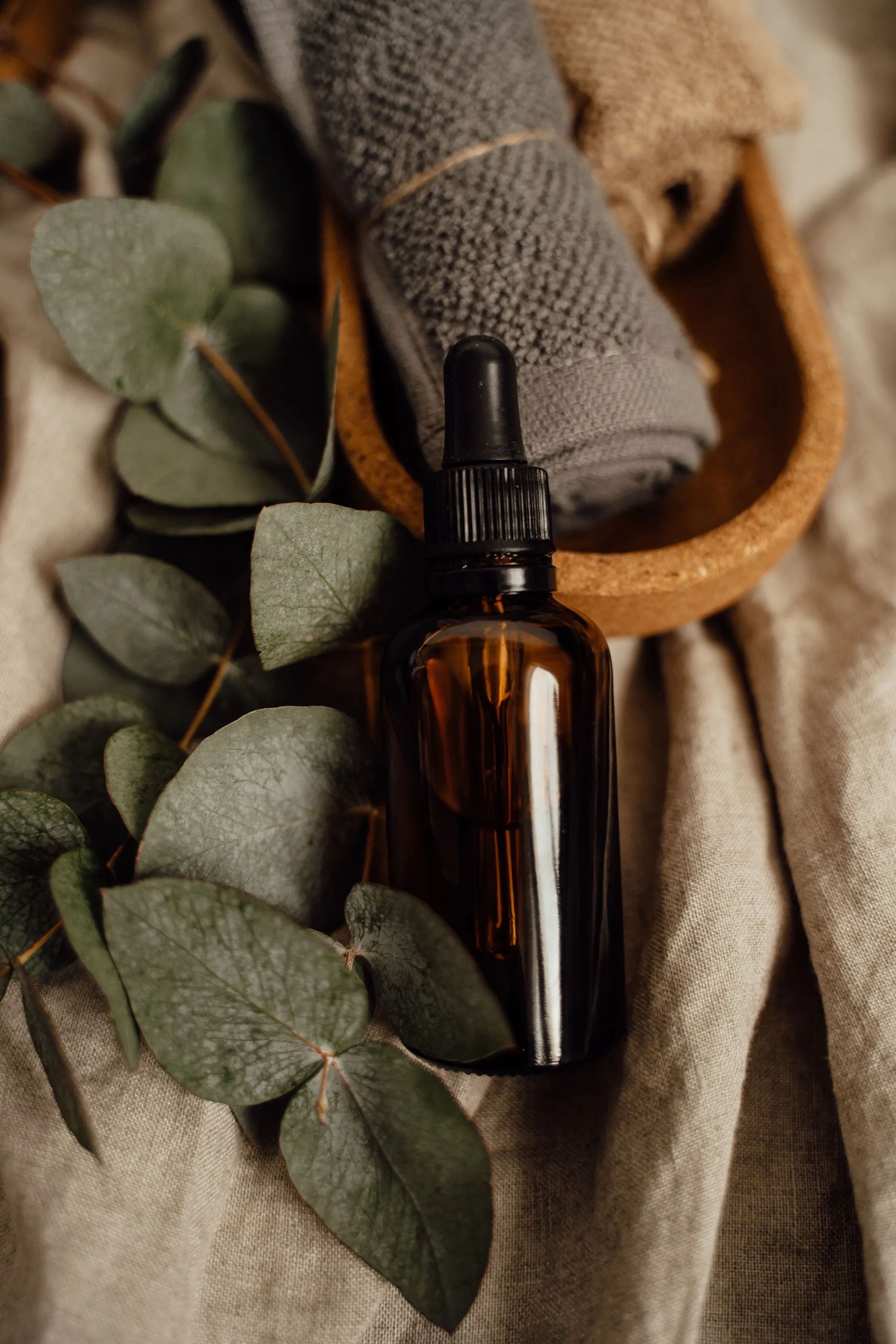 An amber glass oil bottle resting on linen among sprigs of eucalyptus